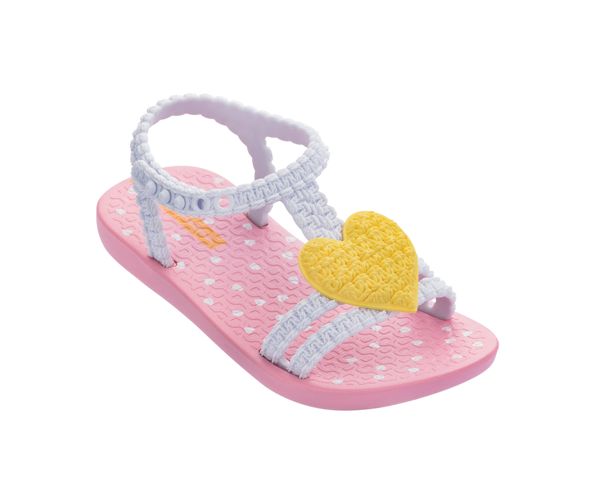 Angled view of a pink and white My First Ipanema Sandal with straps and a yellow crochet heart on top.