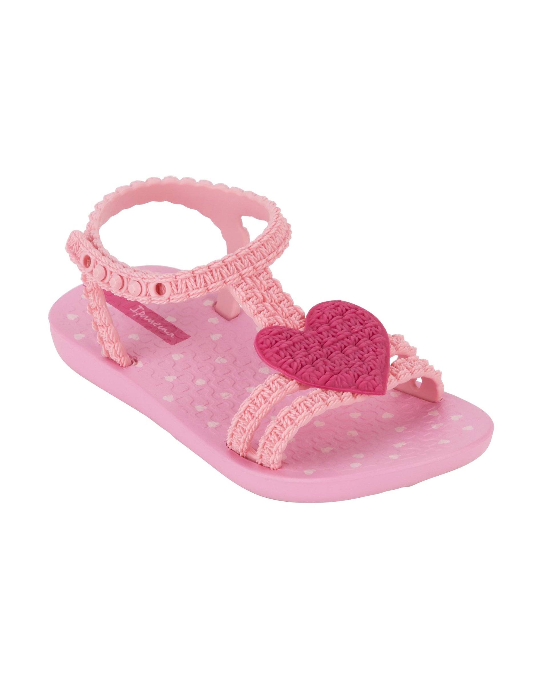 Angled view of a pink Ipanema My First Ipanema baby sandal with pink heart on top and crochet texture .