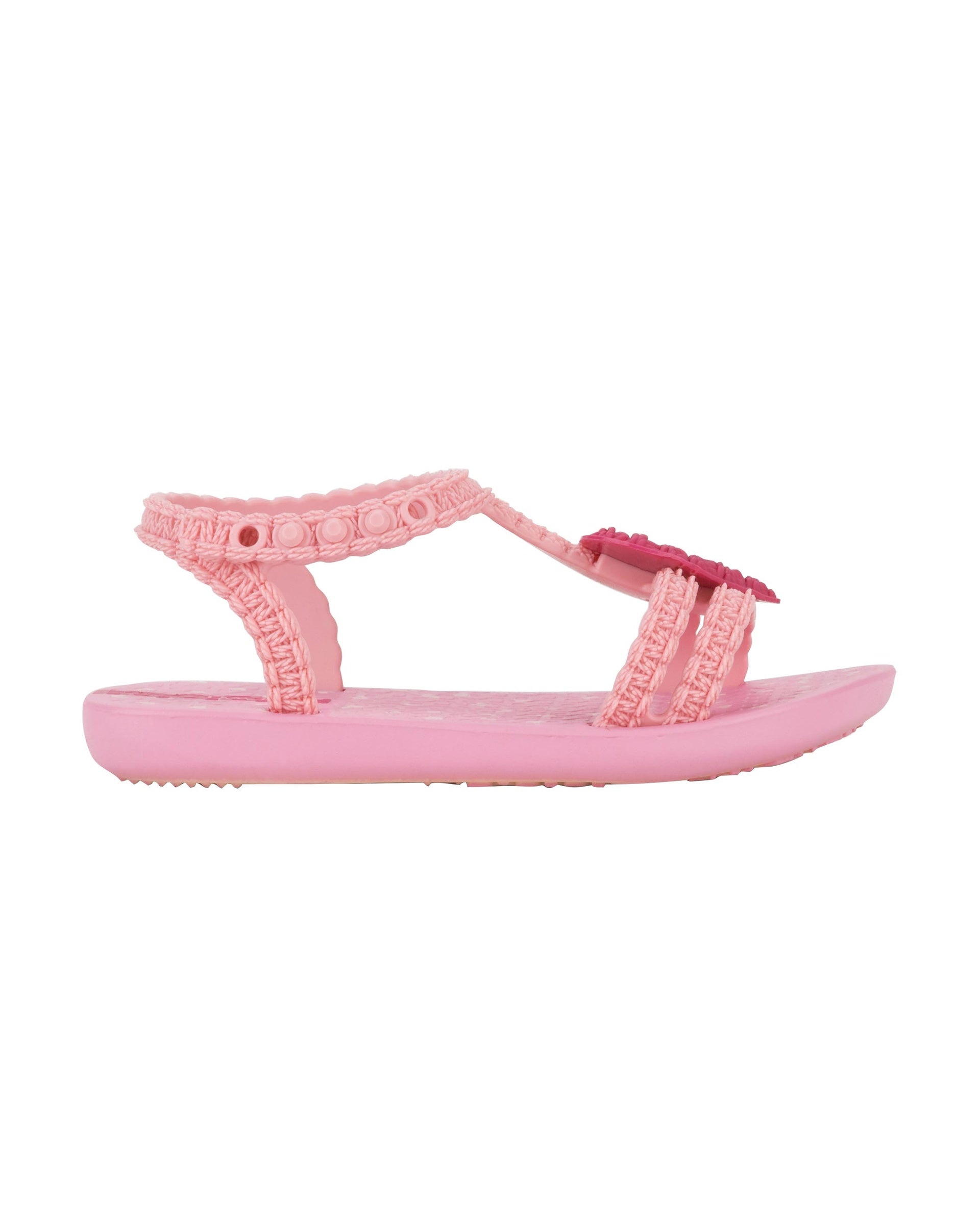 Outer side view of a pink Ipanema My First Ipanema baby sandal with pink heart on top and crochet texture .