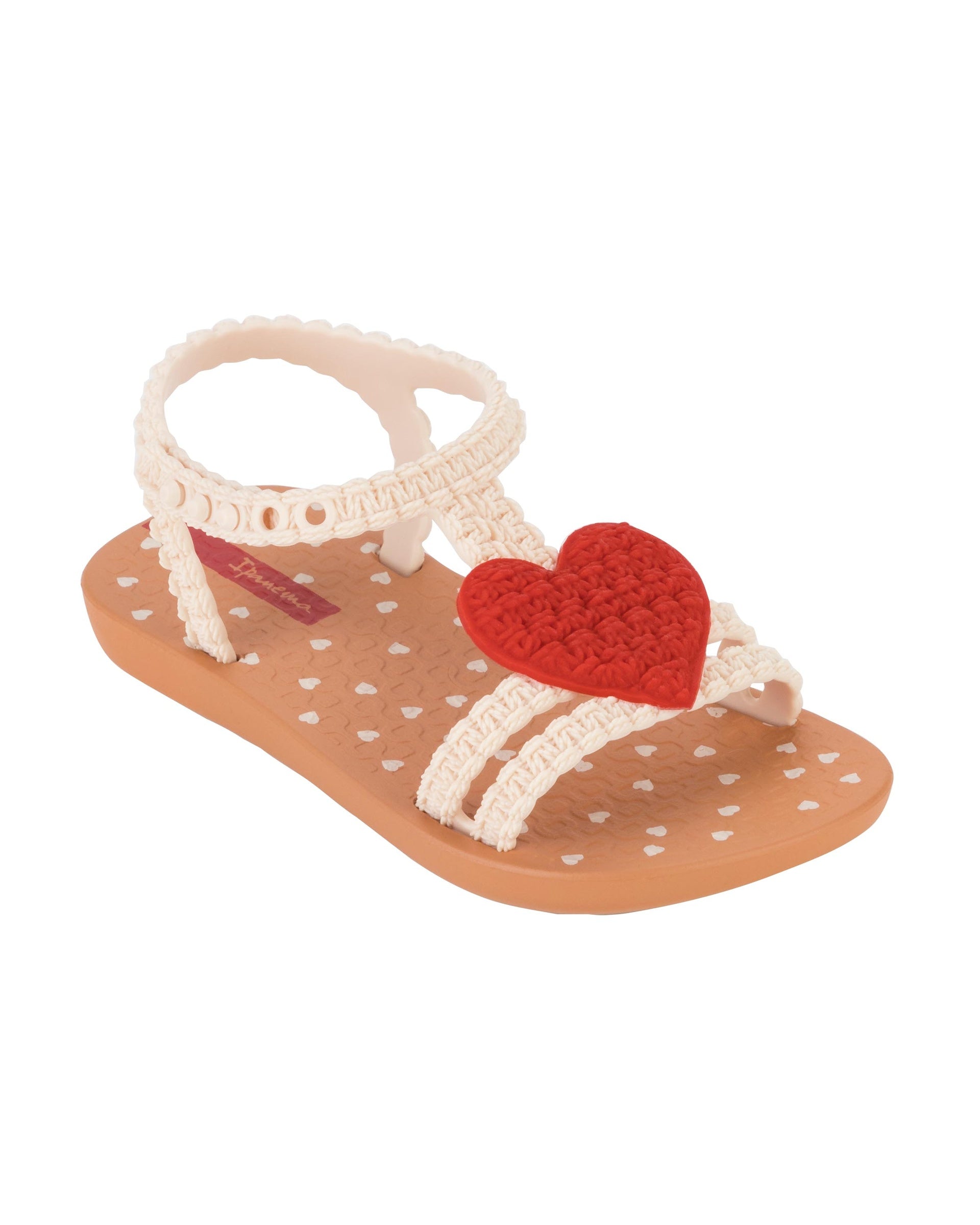 Angled view of a beige Ipanema My First Ipanema baby sandal with red heart on top and crochet texture .