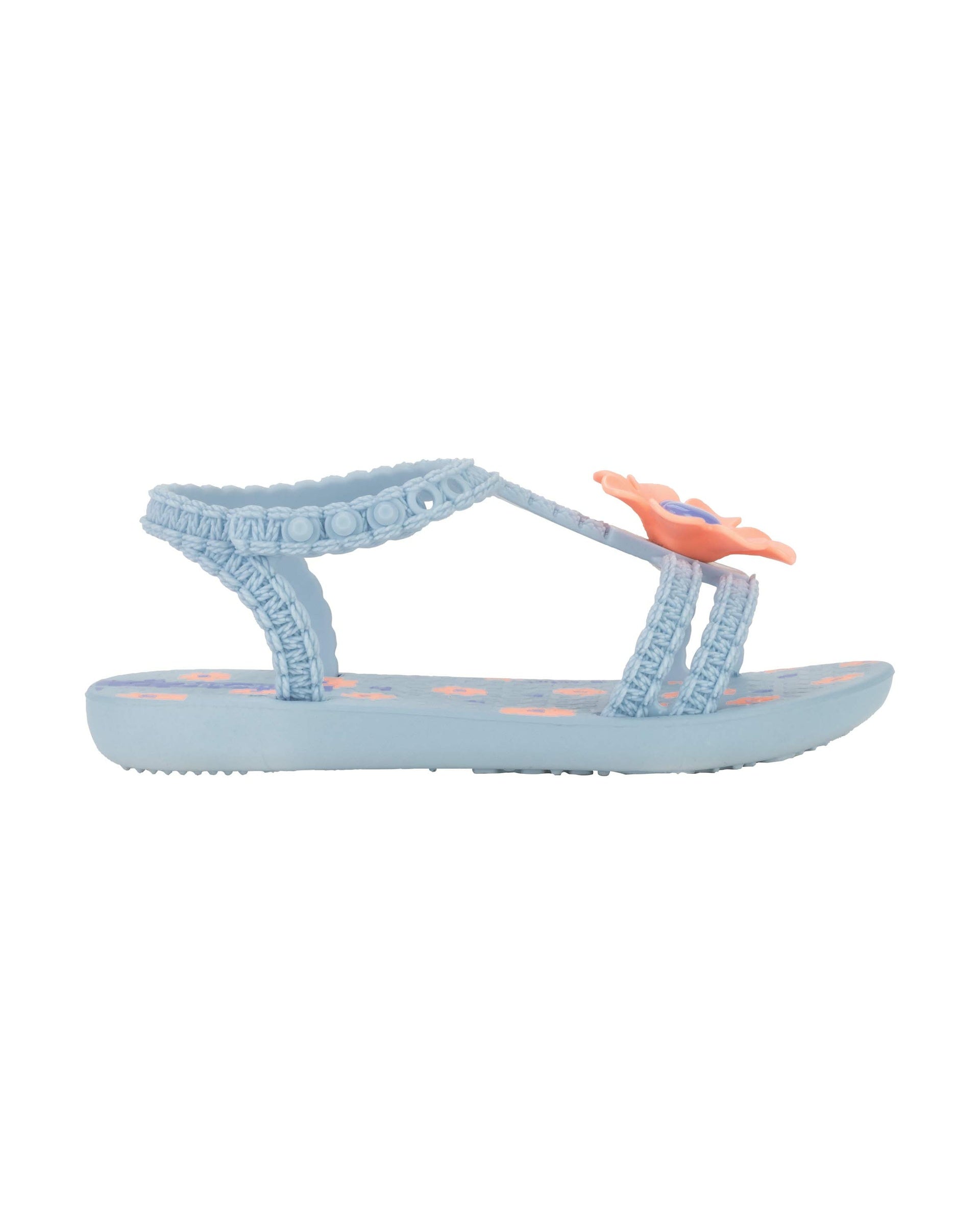 Outer side view of a blue Ipanema Daisy baby sandal with pink flower on top and crochet texture .