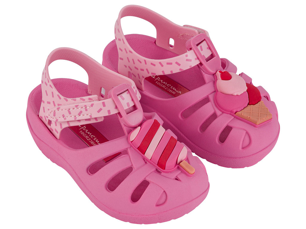Angled view of a pair of pink Ipanema Summer baby fisherman sandal with a popsicle on one upper and an ice cream cone on the other..